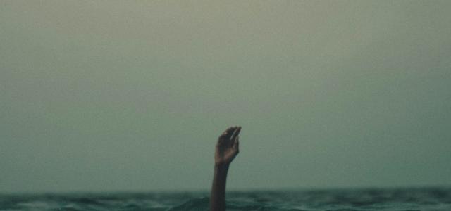 person with hand above water by Mishal Ibrahim courtesy of Unsplash.